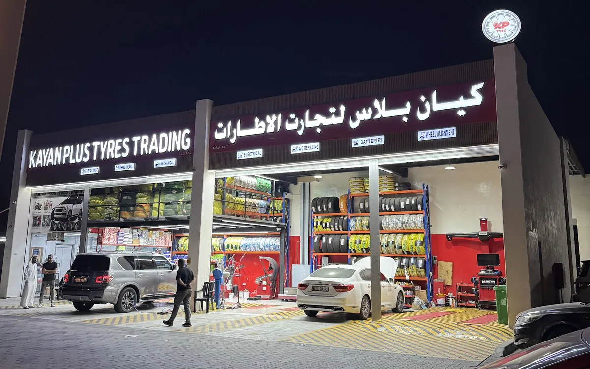 واجهة كيان بلس لتجارة الإطارات في مدينة شخبوط ليلاً مع أرفف التواير والسيارات في منطقة الخدمة